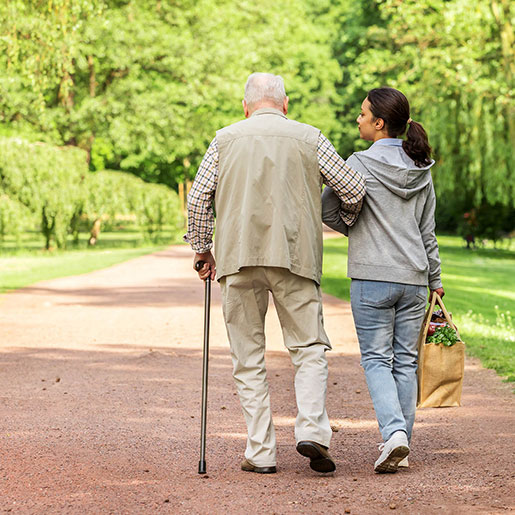 older man with cane walking with caregiver