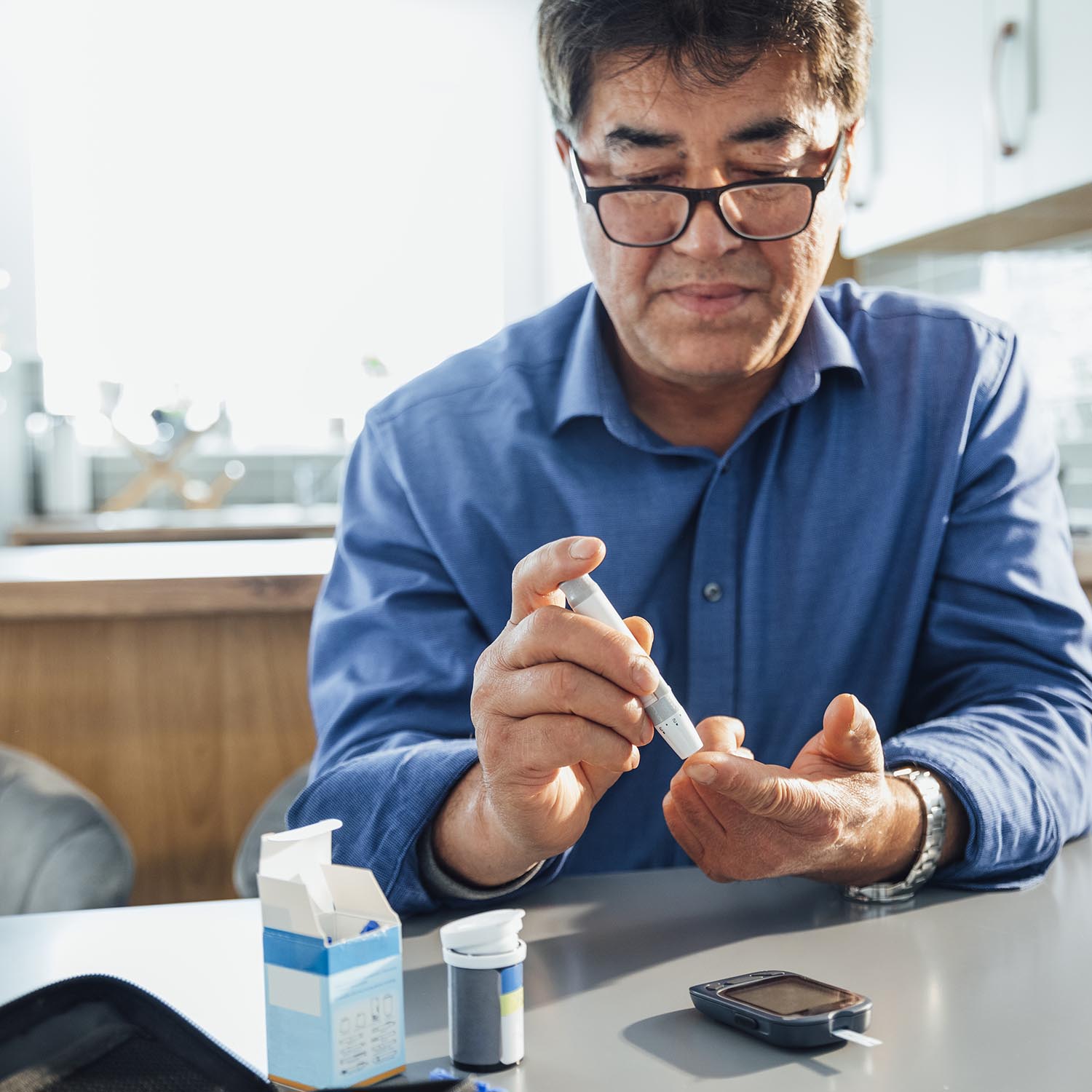 A mature Asian man sitting at a dining table in his kitchen, he is pricking his finger using a glaucometer to test his blood sugar levels, he is managing his diabetes.