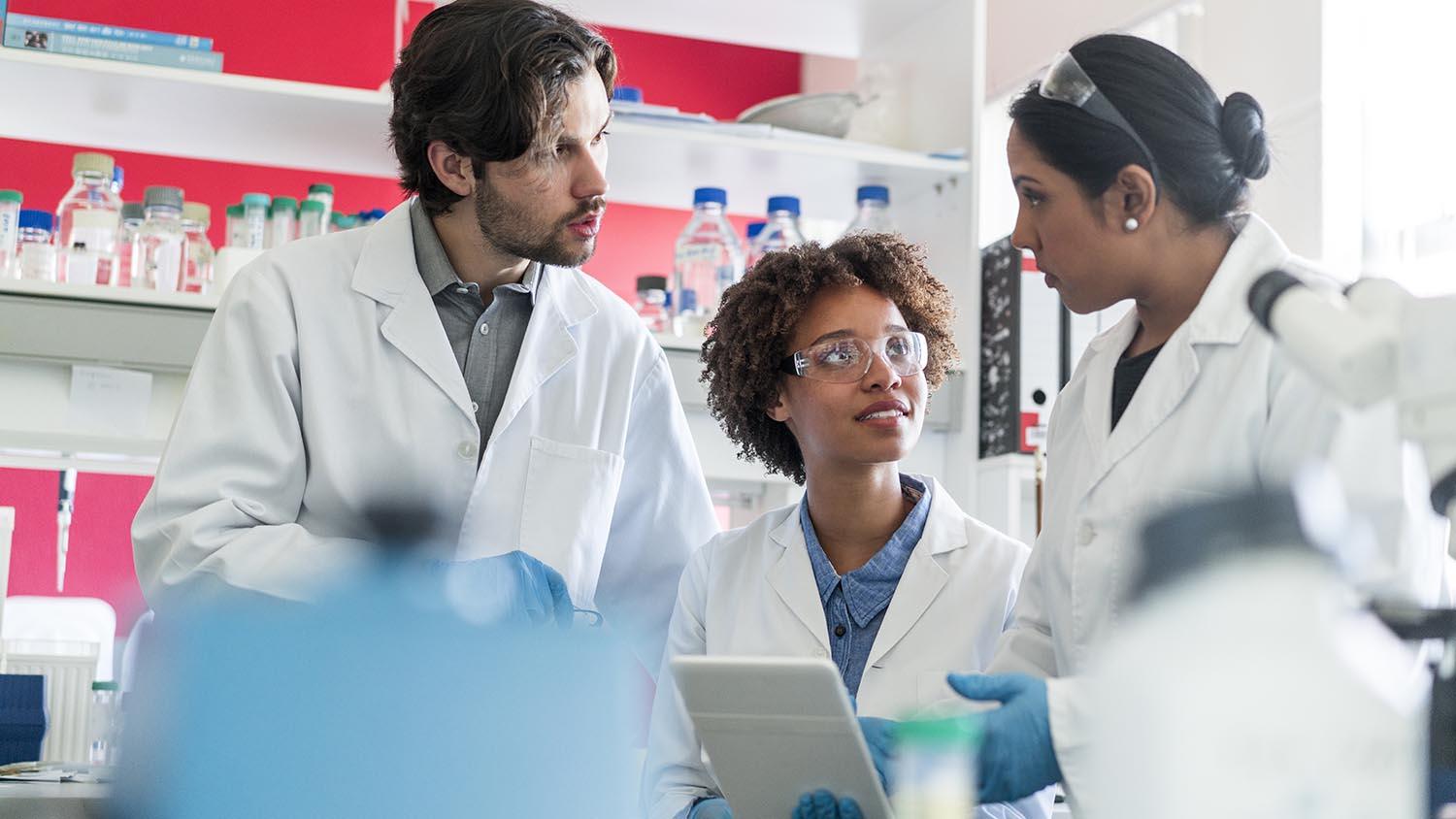 Multi-ethnic scientists discussing over digital tablet. Male and female researchers working together in laboratory. They are in uniforms.