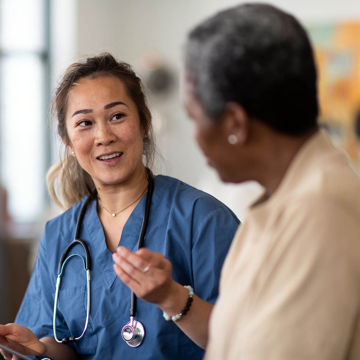 Patient sits on bed while health care professional reviews chart.