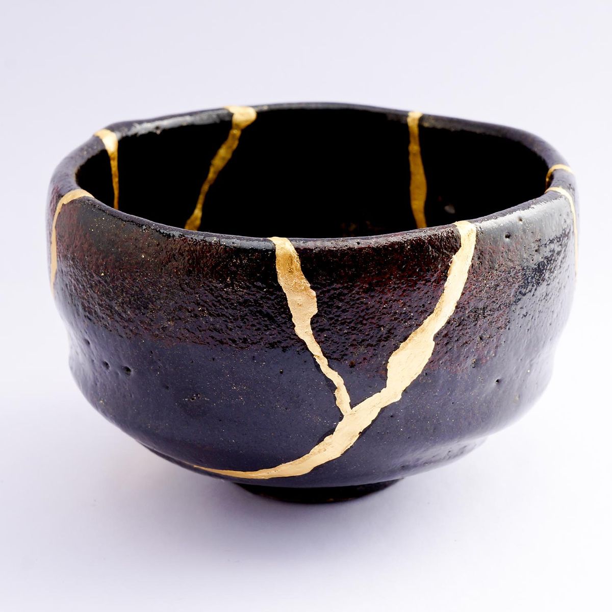 Kintsugi black raku bowl. Gold cracks restoration on old Japanese pottery restored with the antique Kintsugi restoration technique. The beauty of imperfections. japanese pottery repair gold. japanese art of repairing cracks with gold. japanese art of fixing broken pottery