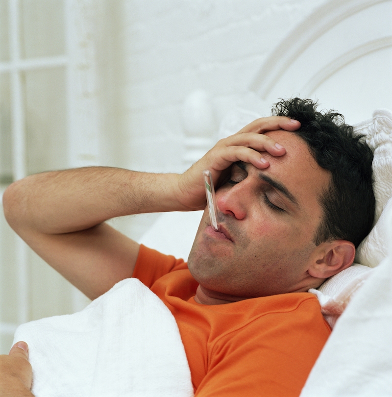 Man sick in bed with thermometer in his mouth