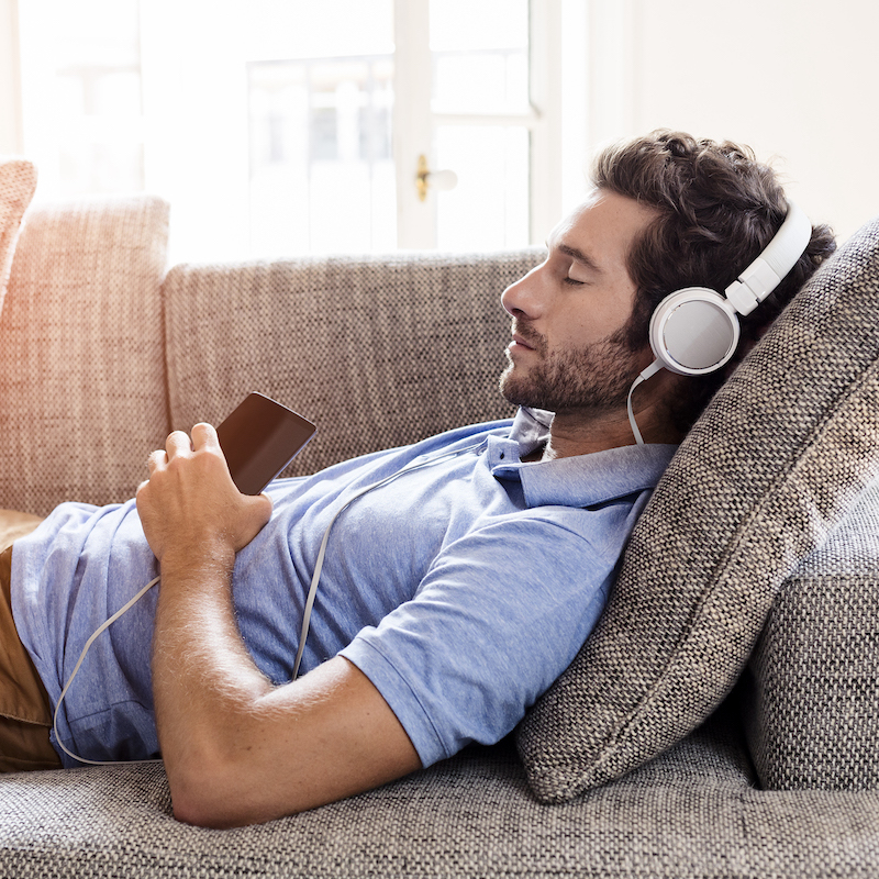 Man with headphones on lying on a couch with his eyes closed