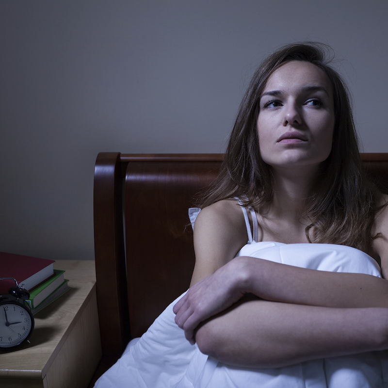 Woman under a blanket sitting up in bed 