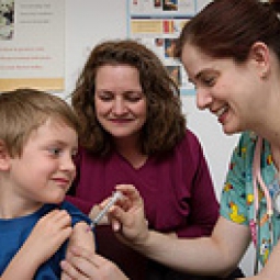 A boy with an adult recieves a shot from a health professional.
