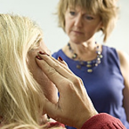 A chiropractor talks to a patient who presses a hand to her temple.