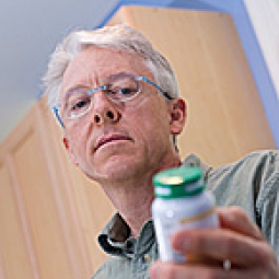 Older man reading the label on a pill bottle.