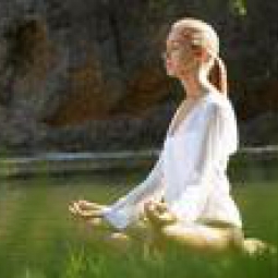 A woman meditates in an open field of flowers.