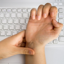 Left hand holds right hand's wrist, indicating pain.