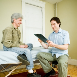 Patient sits on bed while health care professional reviews chart.