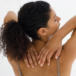 A woman reaches behind her over her sholders to touch her back.