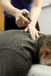 A chiropractic doctor uses an adjustment tool on the back of a patient.